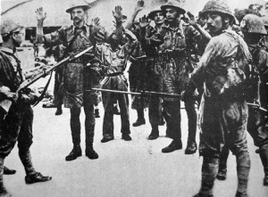 Surrendering troops of the Suffolk Regiment are held at gunpoint by Japanese infantry.